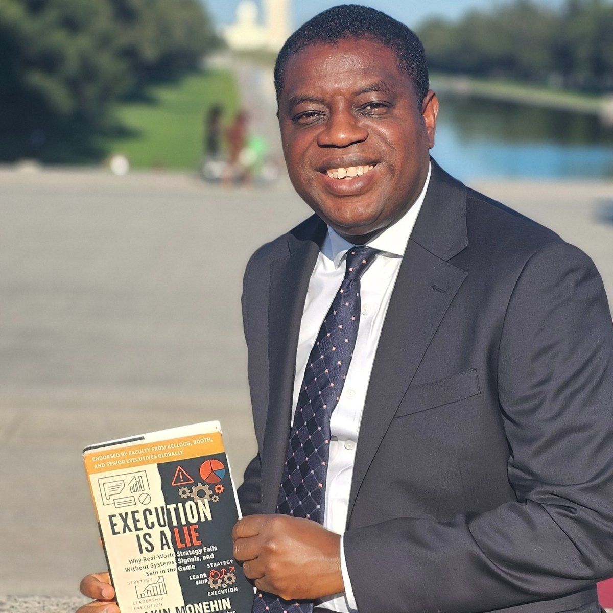 Akin Monehin outdoors, smiling, holding a copy of Execution Is a Lie.